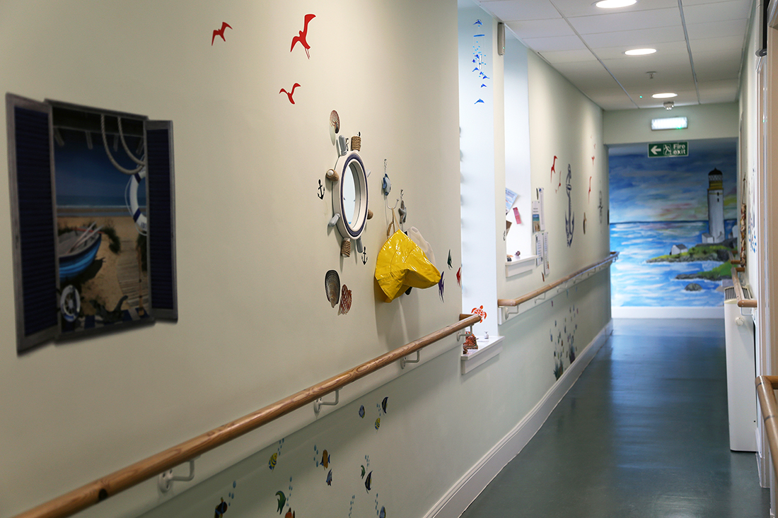 Beach themed hallway with large painting of a lighthouse scene. 
