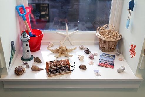 A windowsill set up as a beach scene, with shells and model lighthouse